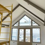 Interior with exposed beams, large triangular windows, and yellow scaffolding in a room under construction