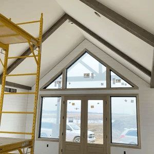 Interior with exposed beams, large triangular windows, and yellow scaffolding in a room under construction