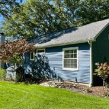 Blue house with white trim, green lawn, and trees in the front yard