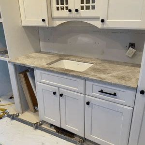 Kitchen under renovation with white cabinets, marble countertop, and unfinished sink area