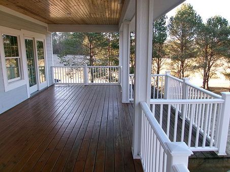 Covered wooden porch with dark deck boards, white railings, and trees visible beyond.