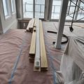 Construction materials on a covered floor in a bright room with windows and scaffolding during renovation