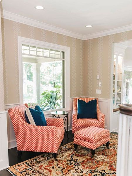 Coral armchair and ottoman in a bright living room with beige walls, patterned rug, and large window.