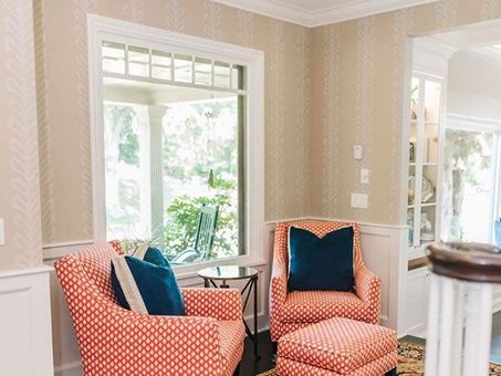 Two coral armchairs with navy pillows in a bright living room by large windows