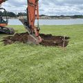 Excavator digging a trench in a grassy field beside a lake