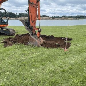 Excavator digging a trench in a grassy field beside a lake