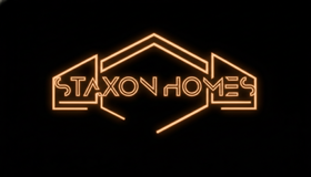 Glowing orange neon “STAXON HOMES” logo on a black background