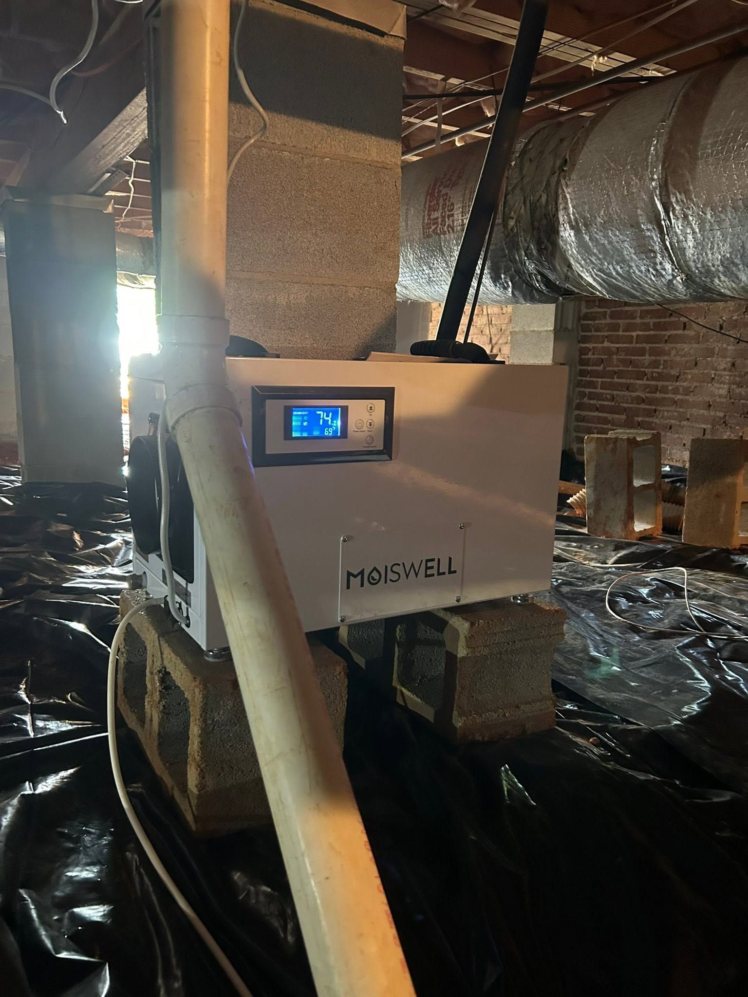 Furnace room with a digital control unit and large insulated ductwork on a reflective black floor.