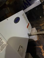 White appliance or box with label, leaning in a cluttered storage area with dark background.