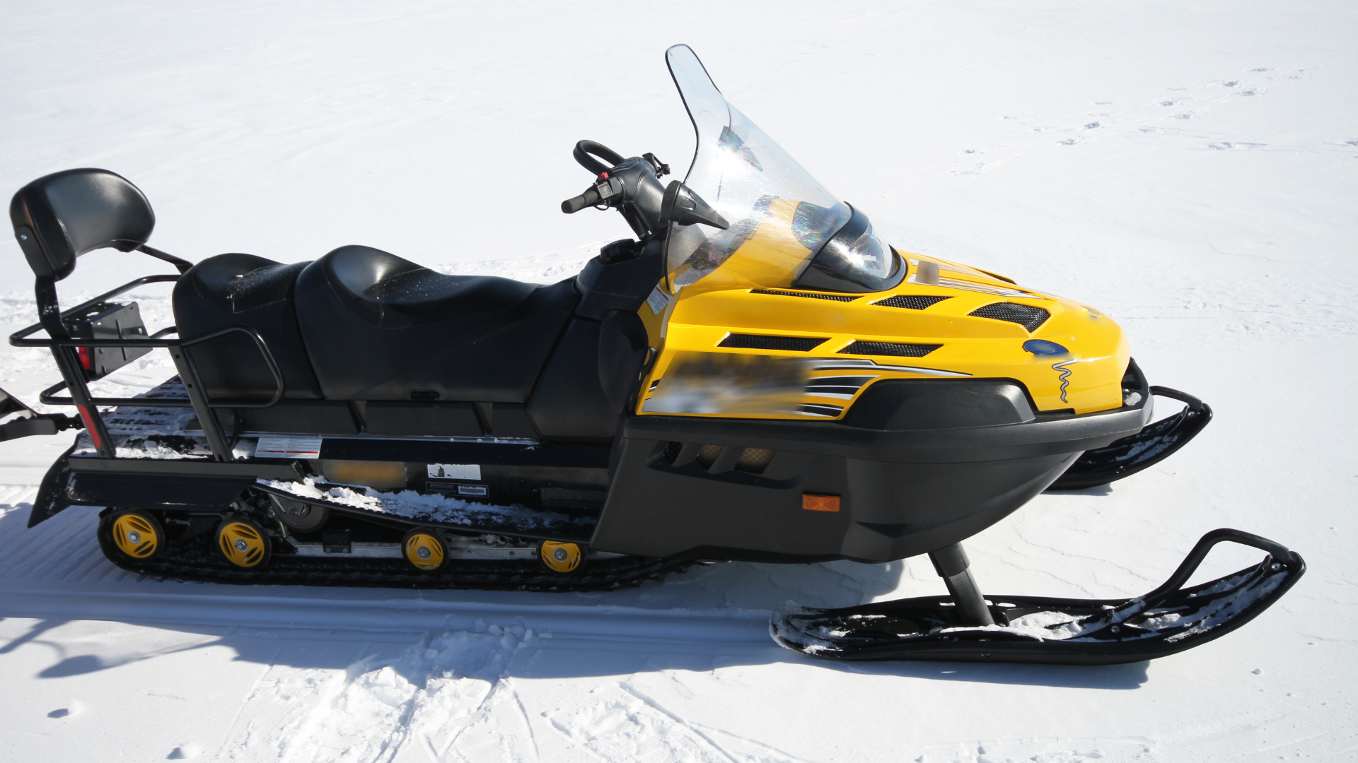 Yellow and black snowmobile parked on snow, side view