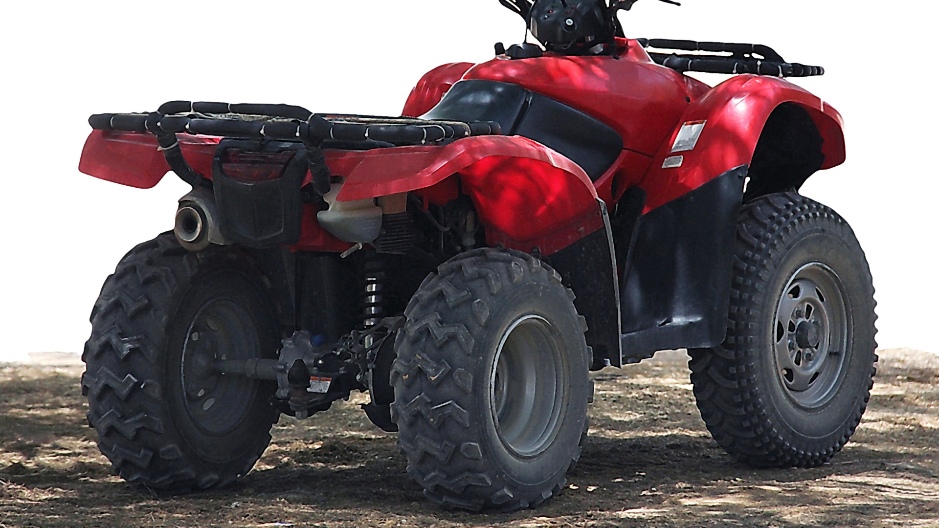 Red ATV parked on a dirt surface, viewed from the rear, with large knobby tires.