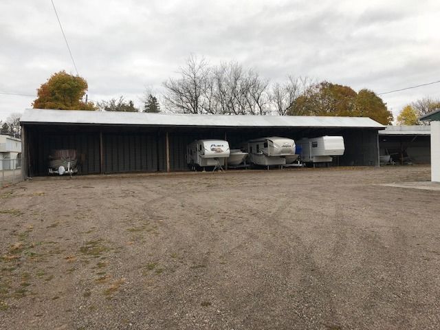 Open-sided carport with three RV trailers parked on a gravel lot under cloudy skies