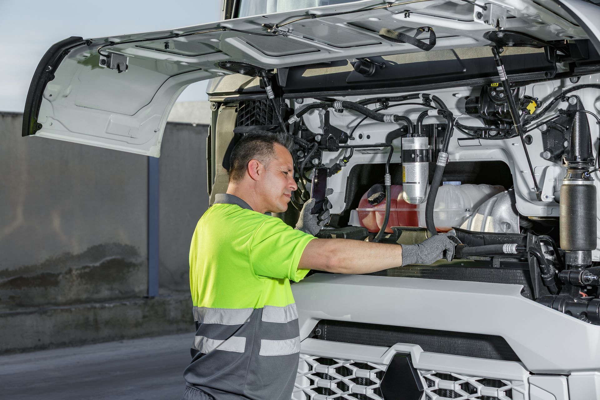 Truck driver inspecting engine of white semi-truck on roadside.