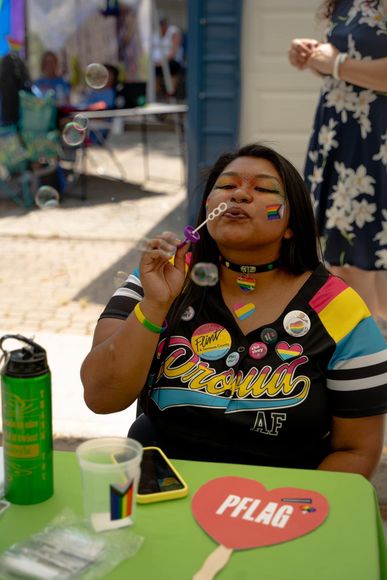 Person blowing bubbles outdoors at a picnic table with a red heart sign and green drink container