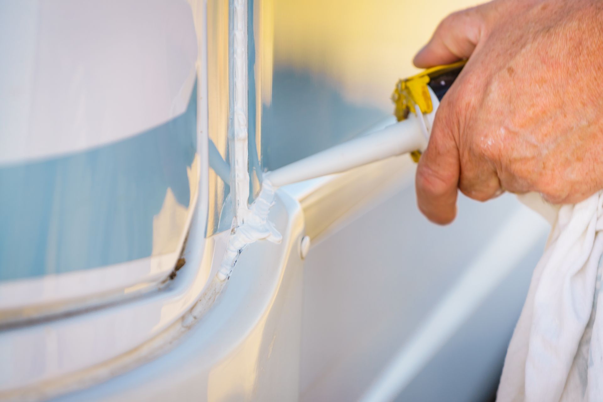 A Hand Holds a Caulking Gun, Applying White Sealant — Coast to Country Caravan Repairs In Port Macquarie, NSW