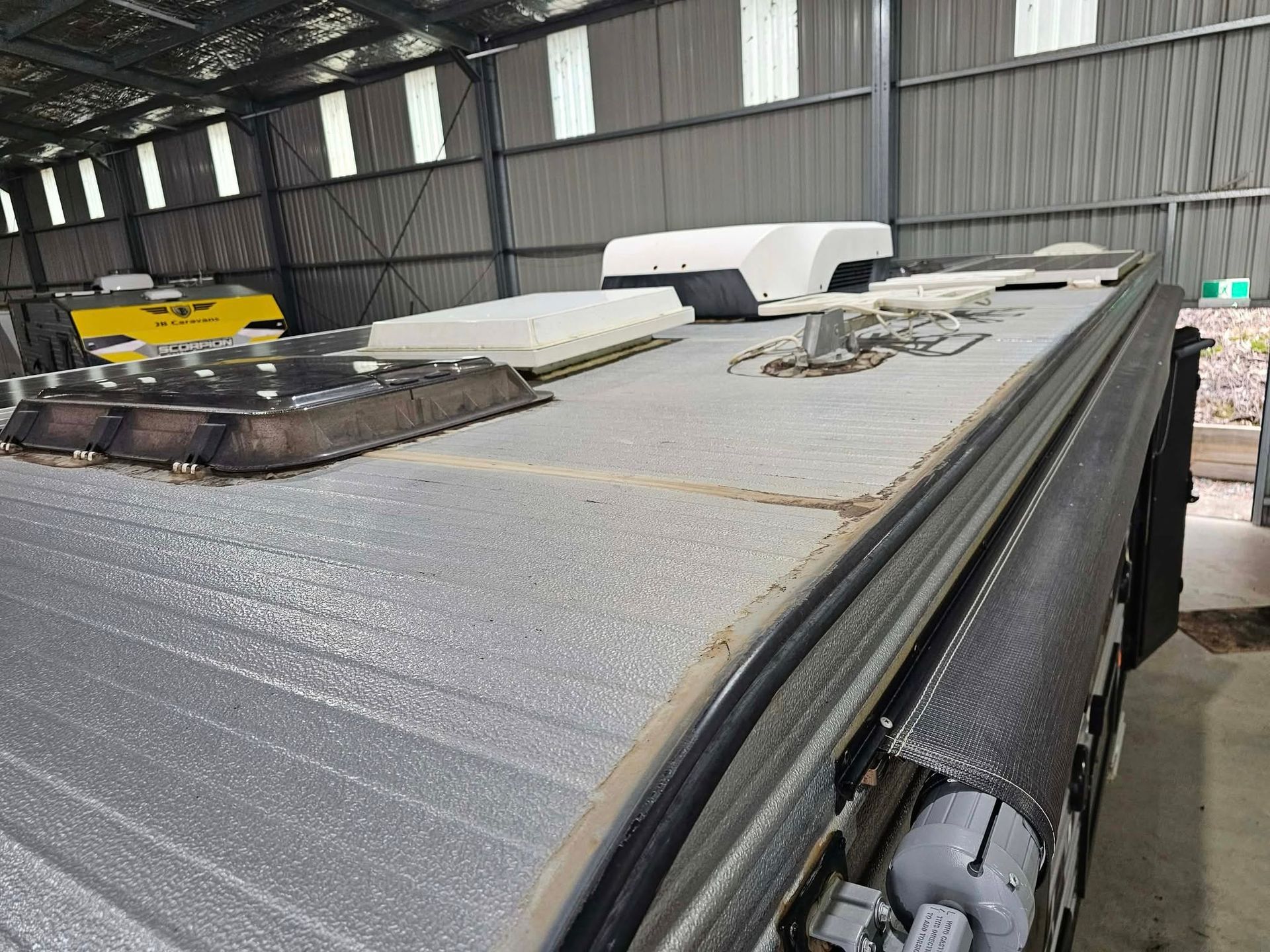 A high-angle view of a recreational vehicle roof featuring a vent, air conditioning unit, and a rolled-up awning — Coast to Country Caravan Repairs In Port Macquarie, NSW