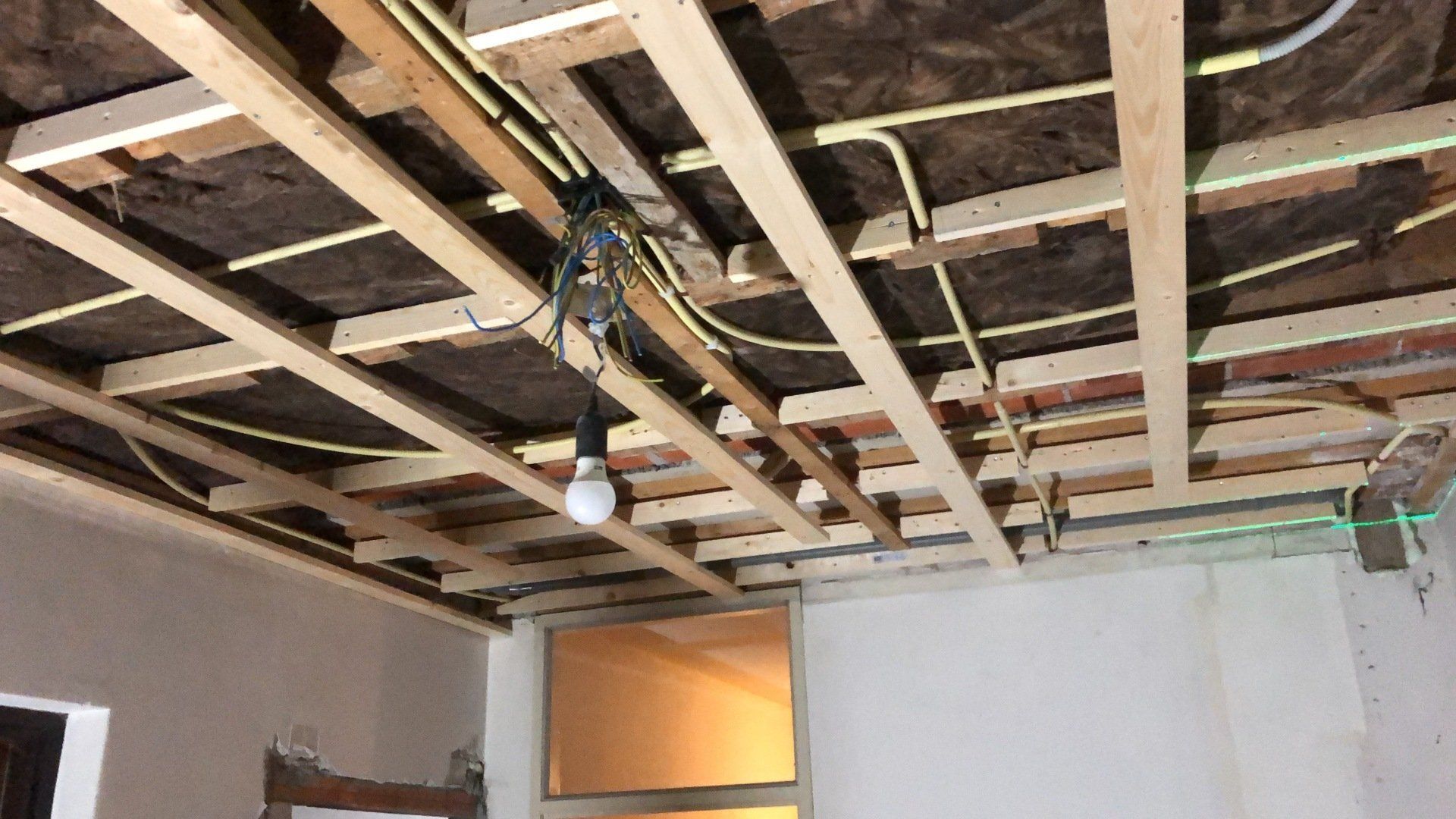Zichtbare plafondconstructie met bedrading en een hangende gloeilamp in een onafgewerkte kamer.