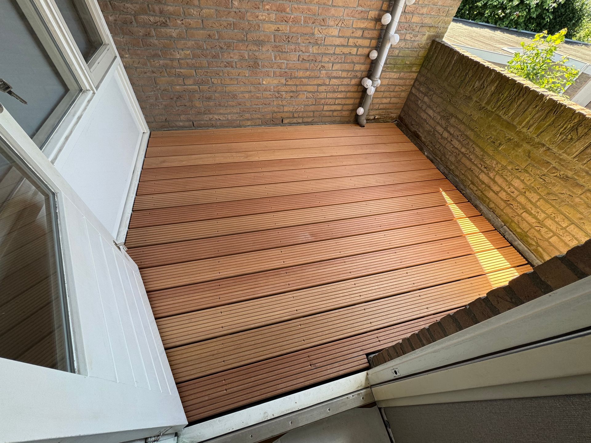 Een klein bakstenen terras met een gebogen houten vlonder, omgeven door muren en met een deur die erop uitkomt.