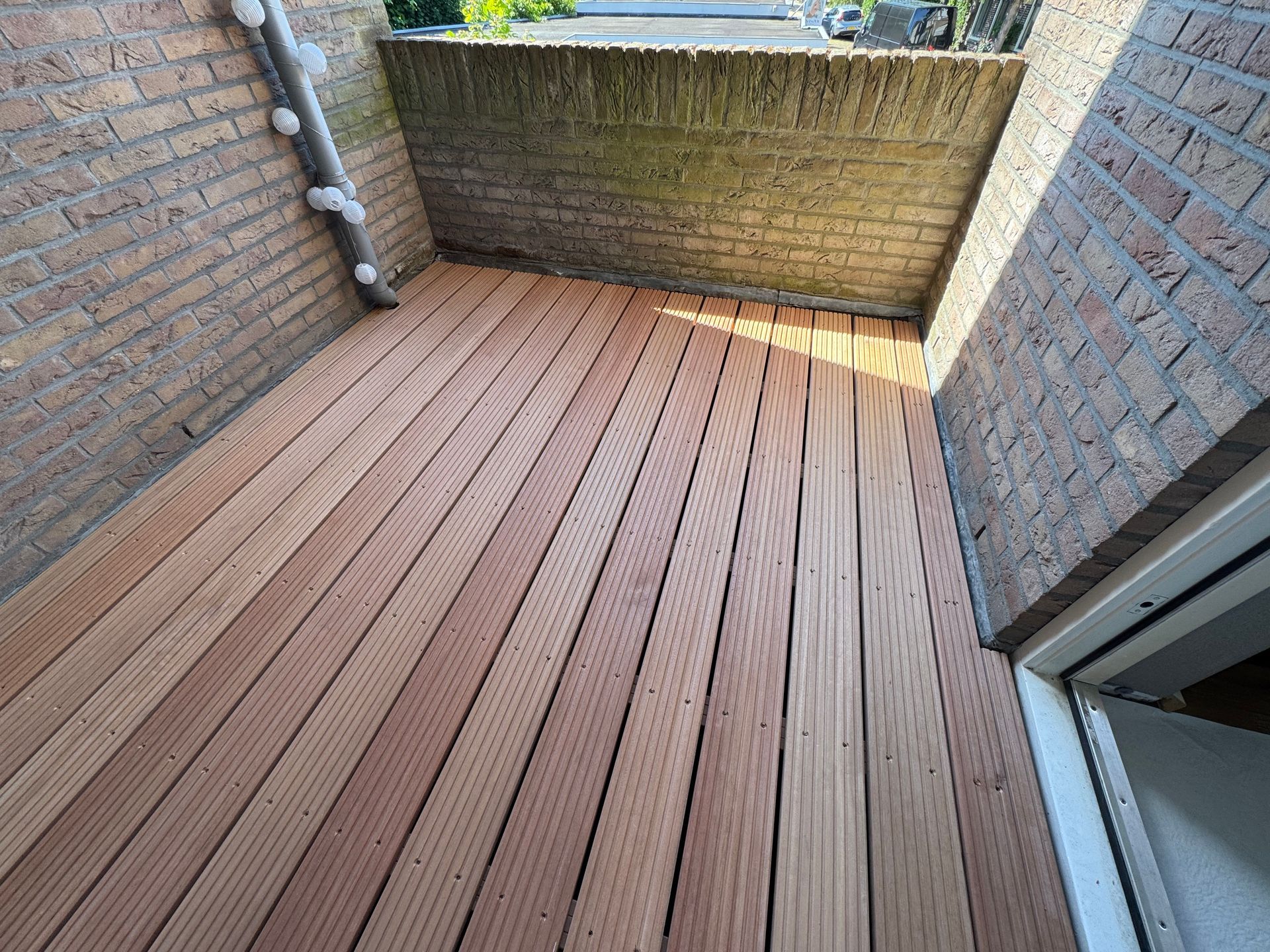Smalle, met bakstenen ommuurde binnenplaats met een houten terras en een lage, met mos begroeide muur aan het uiteinde.