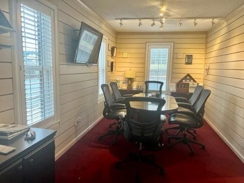 Small meeting room with a black table, chairs, wall TV, white shiplap walls, and red carpet.