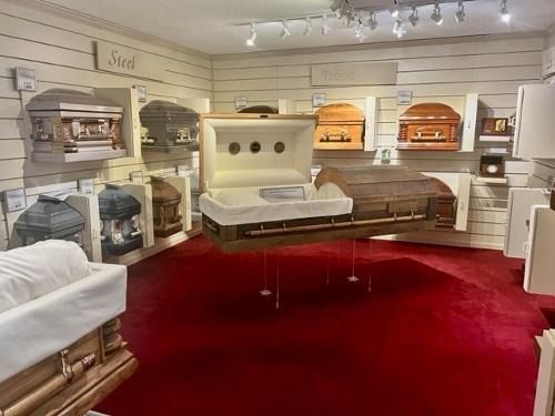 Casket showroom with white display cases, wooden caskets, and a red carpeted floor