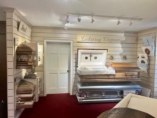 Interior of a funeral home showroom with a casket display and burgundy carpet.