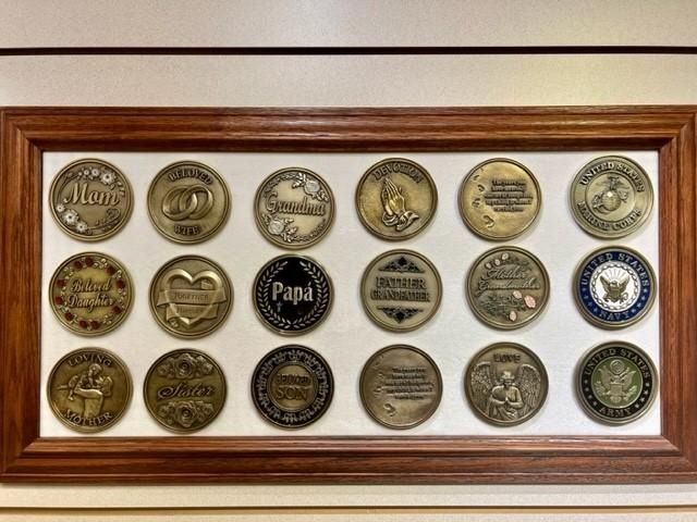 Framed display of assorted decorative metal bottle caps or tokens arranged in a grid.