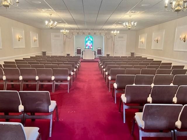 Empty church sanctuary with rows of brown pews, a red carpet aisle, and a stained-glass window at the front