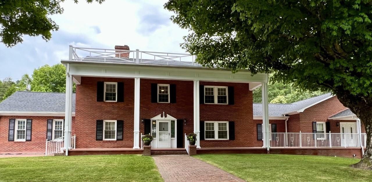 Historic red-brick house with white columns, black shutters, and a front walkway under a cloudy sky