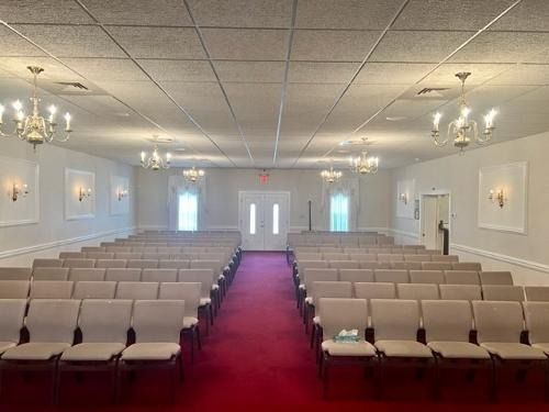 Empty church hall with rows of beige chairs and a red carpet aisle leading to double doors