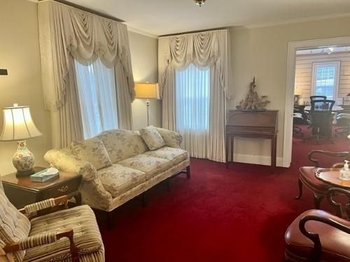 Elegant living room with red carpet, cream sofa, lamps, draped windows, and fireplace mantel