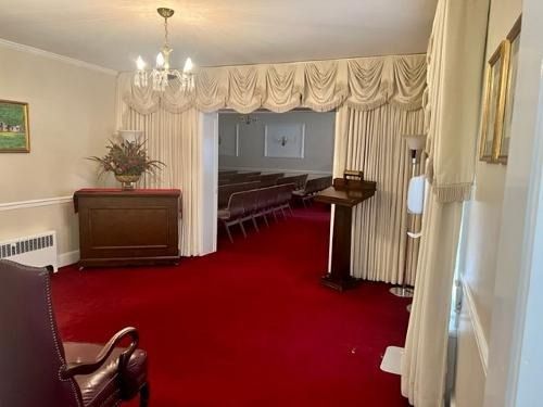 Red-carpeted church interior with pews, chandelier, and a lectern under draped curtains