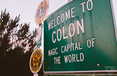 Green roadside sign reading “Welcome to Colon, Magic Capital of the World” with city seals.