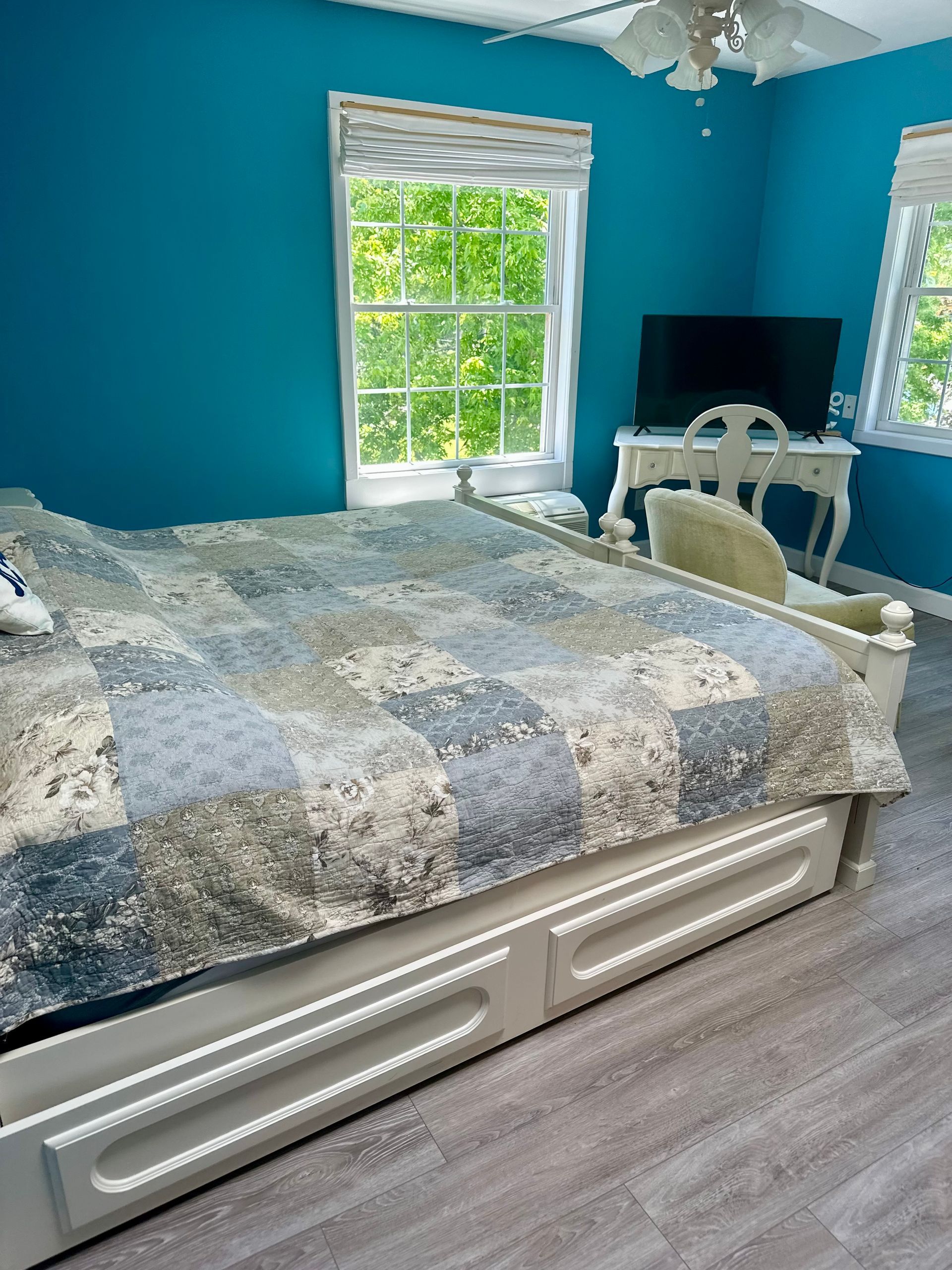 Bright blue bedroom with a bed, desk, and windows letting in daylight