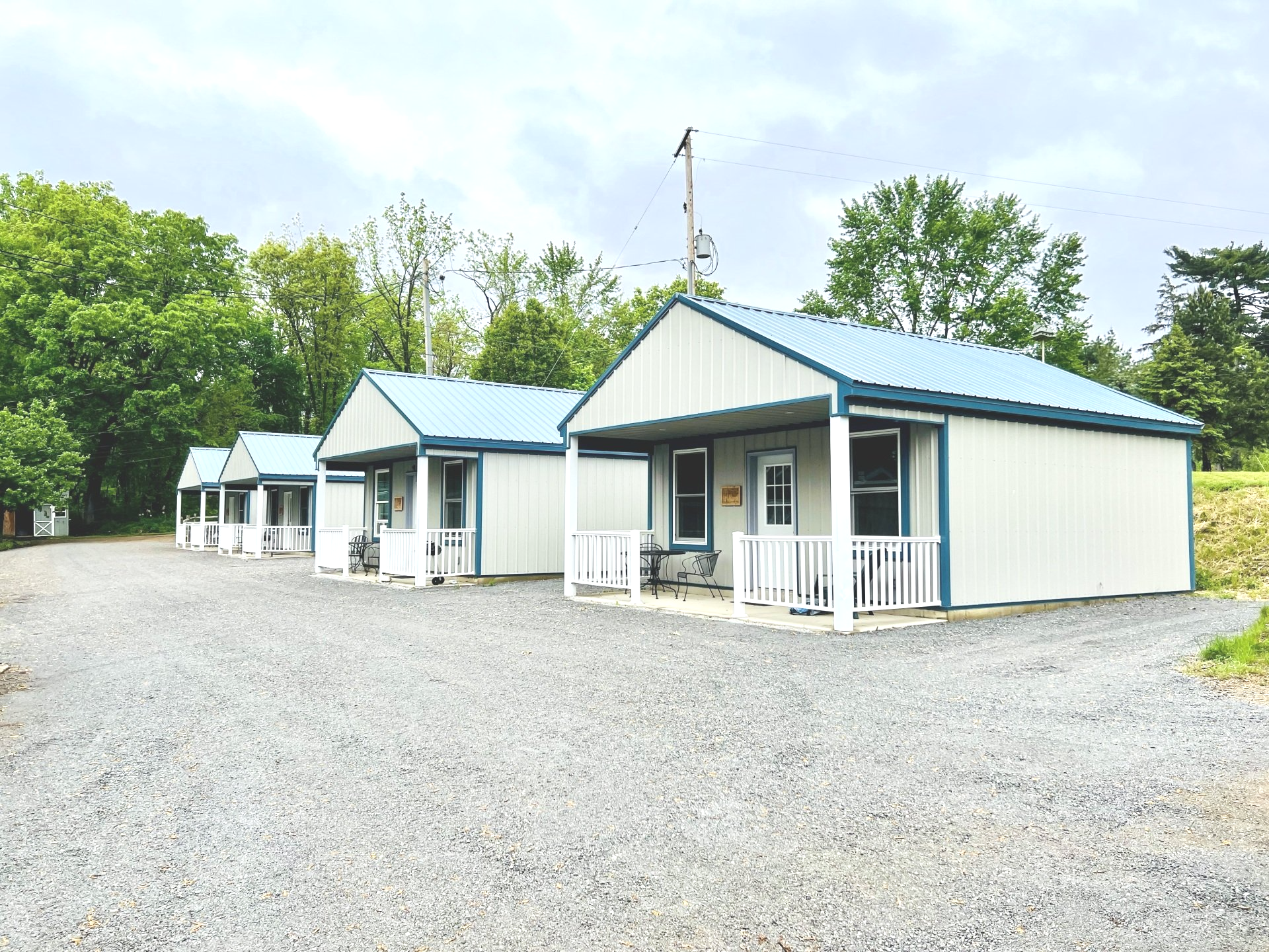 Small white cabins with blue roofs on a gravel lot surrounded by trees