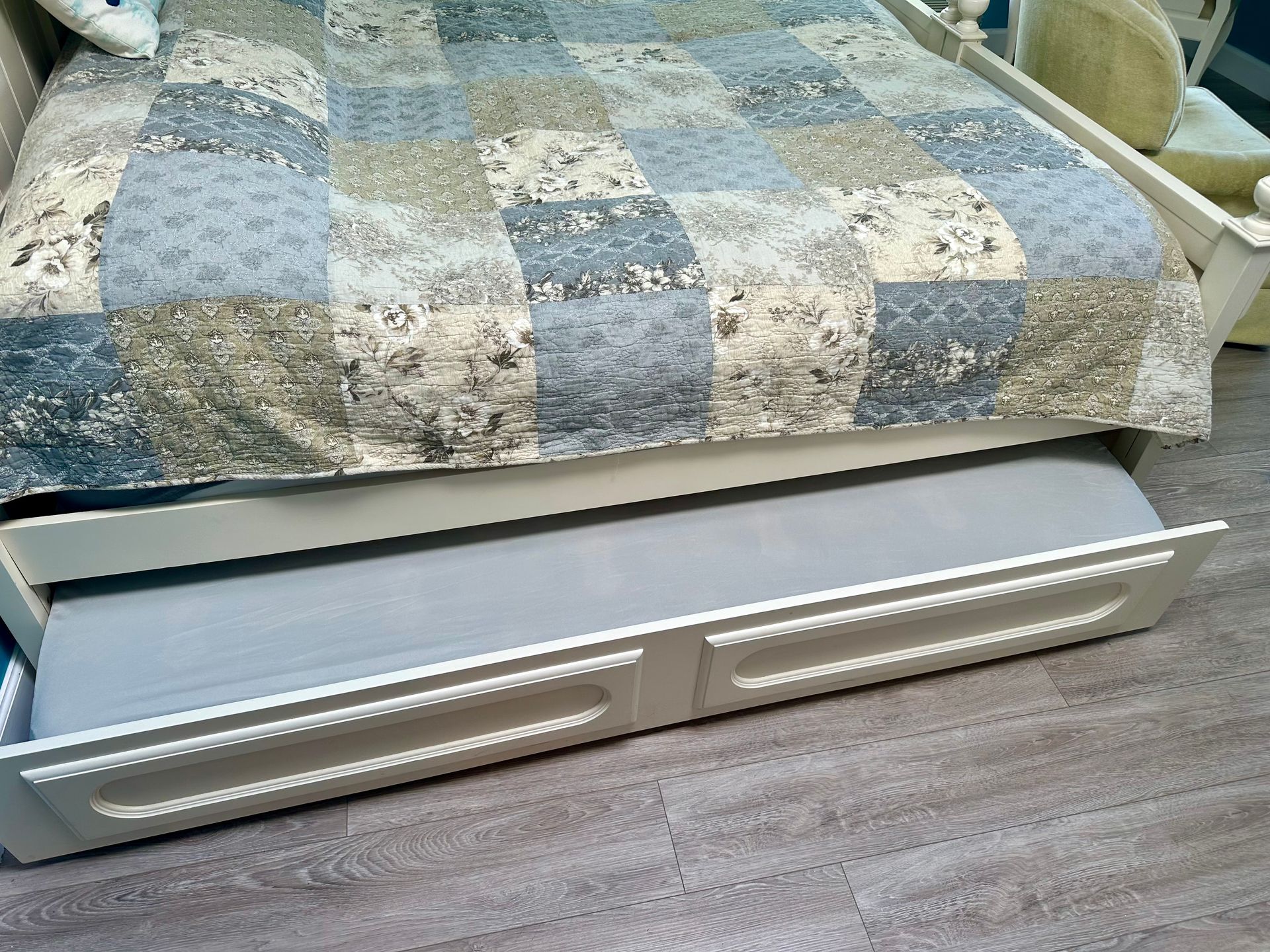 White under-bed storage drawers beneath a bed with a blue-and-cream patchwork quilt on a wood floor