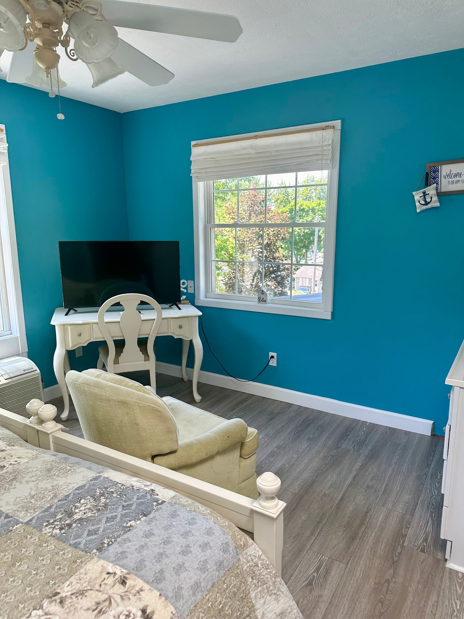 Bright turquoise home office with desk, TV, window, and cream chair on gray floor