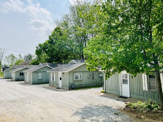 Row of small weathered white cottages along a gravel path under leafy green trees