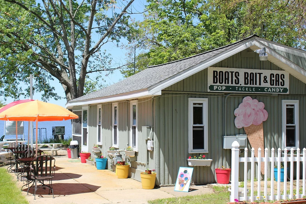 Small roadside boat rental and gift shop with a white fence, colorful pots, and an ice cream sign.