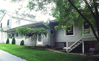 White house with porch and stairs beside a tree-lined street