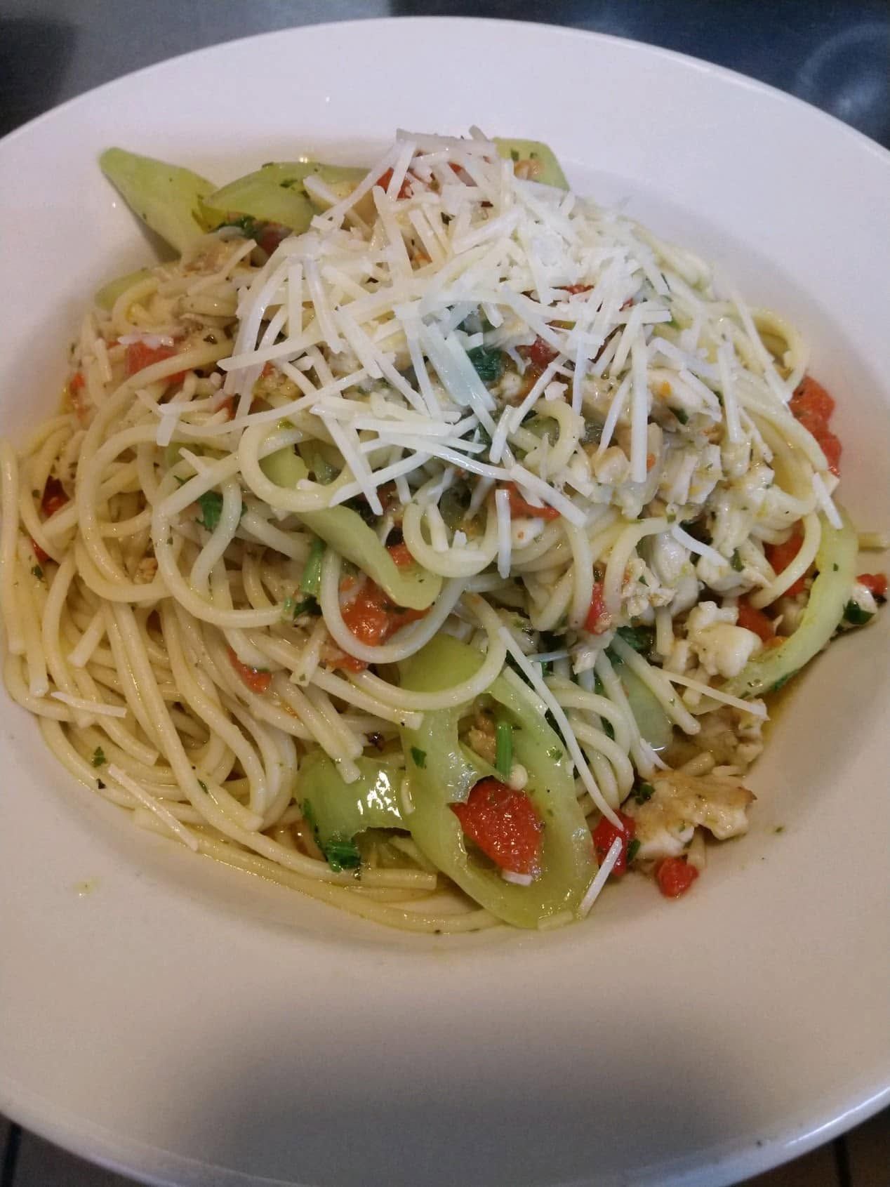 Pasta salad topped with grated cheese and vegetables in a white bowl
