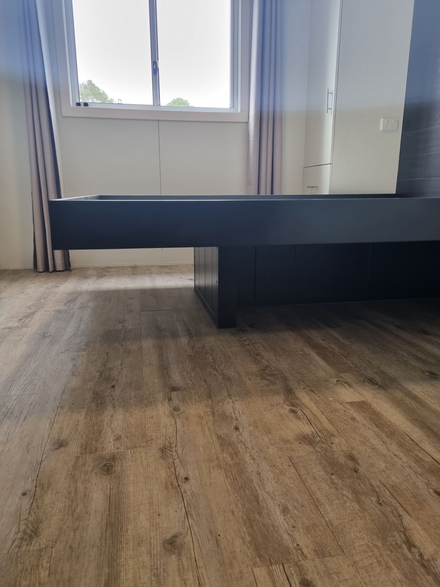 Wooden Floor With a Black Bed Frame, a Window, and Curtains — Taylormade Constructions & Renovations In Goodger, QLD