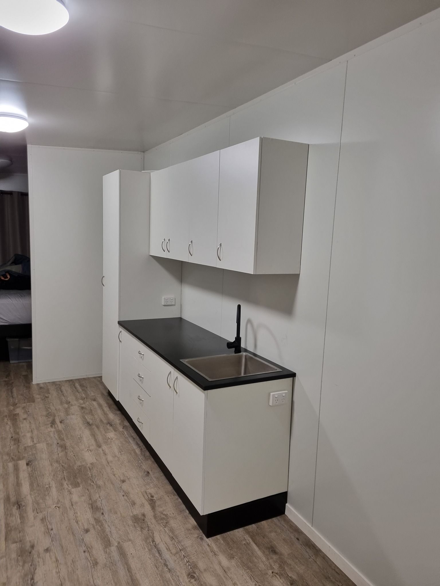 A Small White Kitchenette With Cabinets and Black Countertop — Taylormade Constructions & Renovations In Memerambi, QLD