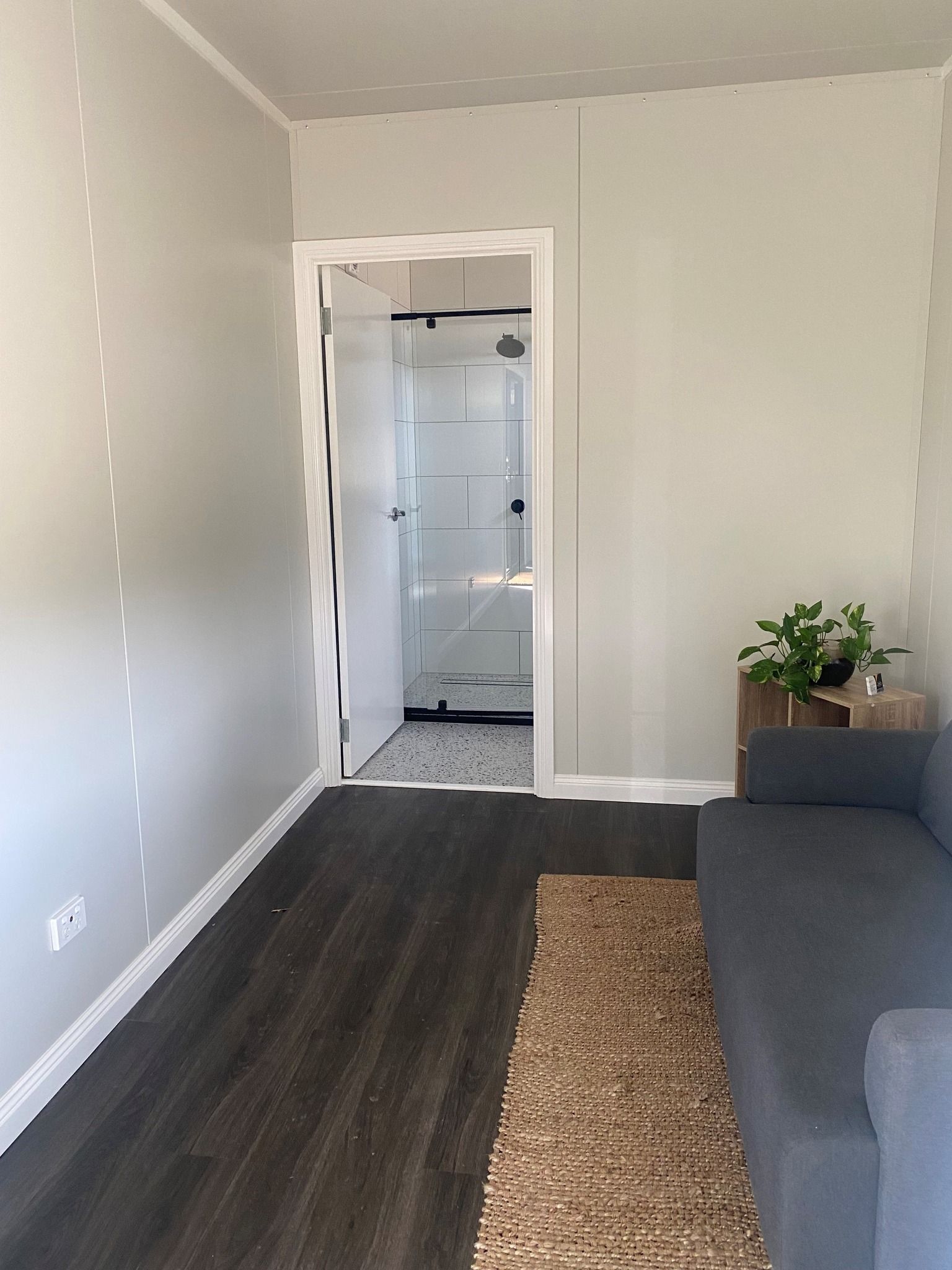 A Small Room With Dark Flooring, a Grey Couch, and an Open Doorway — Taylormade Constructions & Renovations In Yarraman, QLD