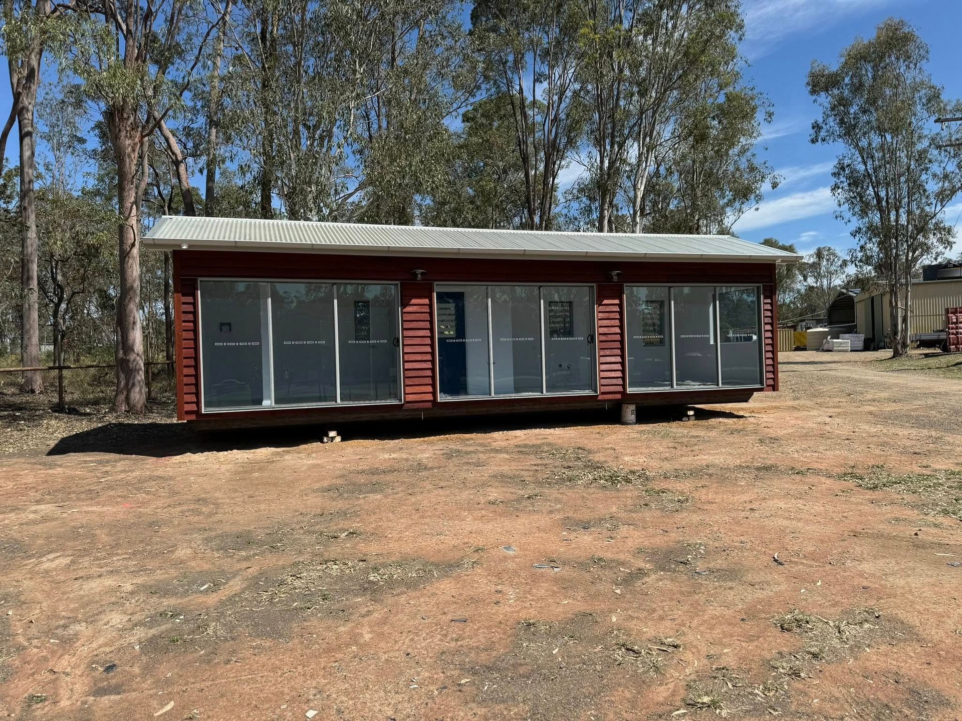Red Cabin With Glass Walls on a Brown Dirt Field — Taylormade Constructions & Renovations In Nanango, QLD