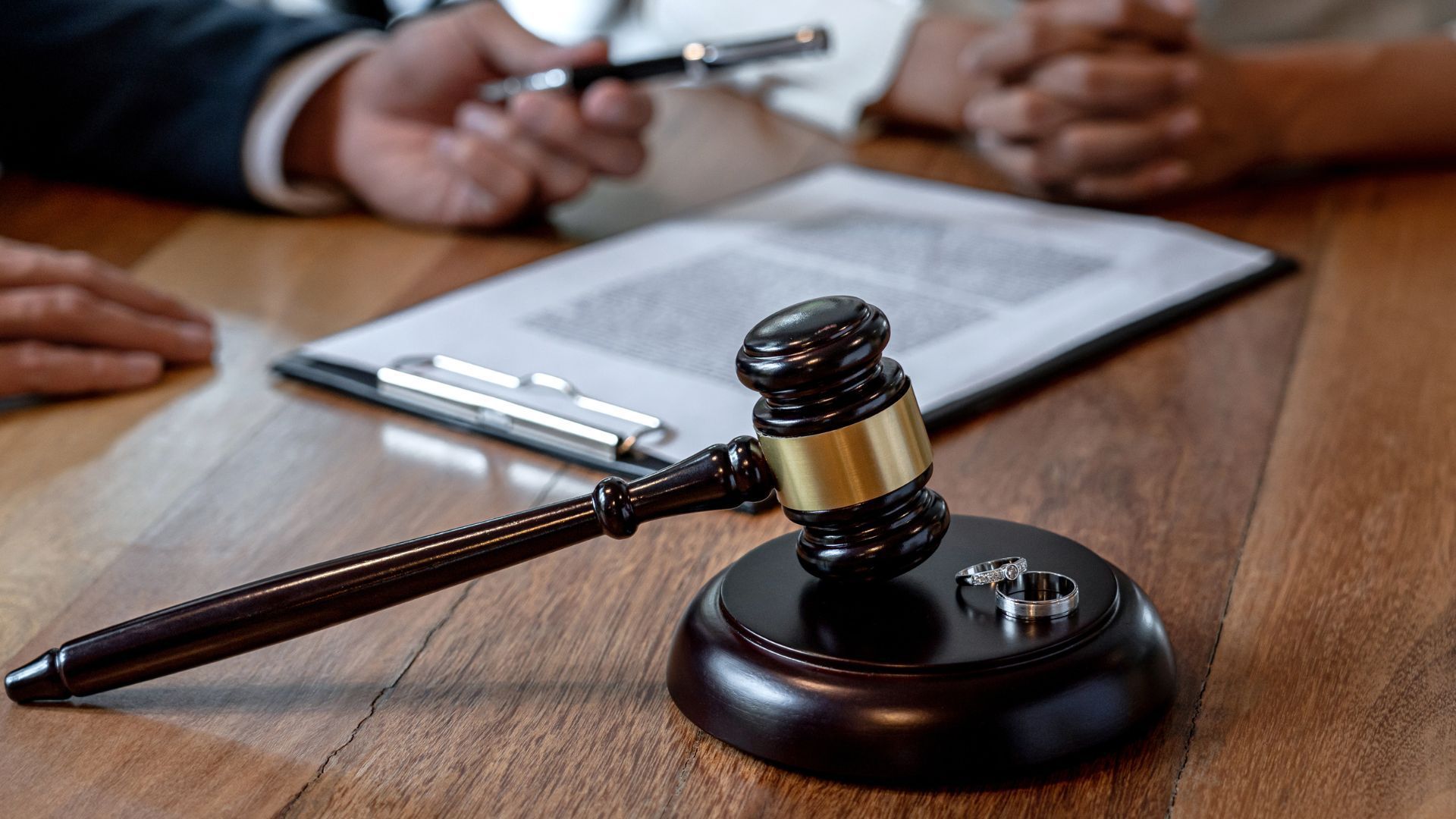 Gavel on block with wedding rings; couple and legal documents on table, divorce consultation.