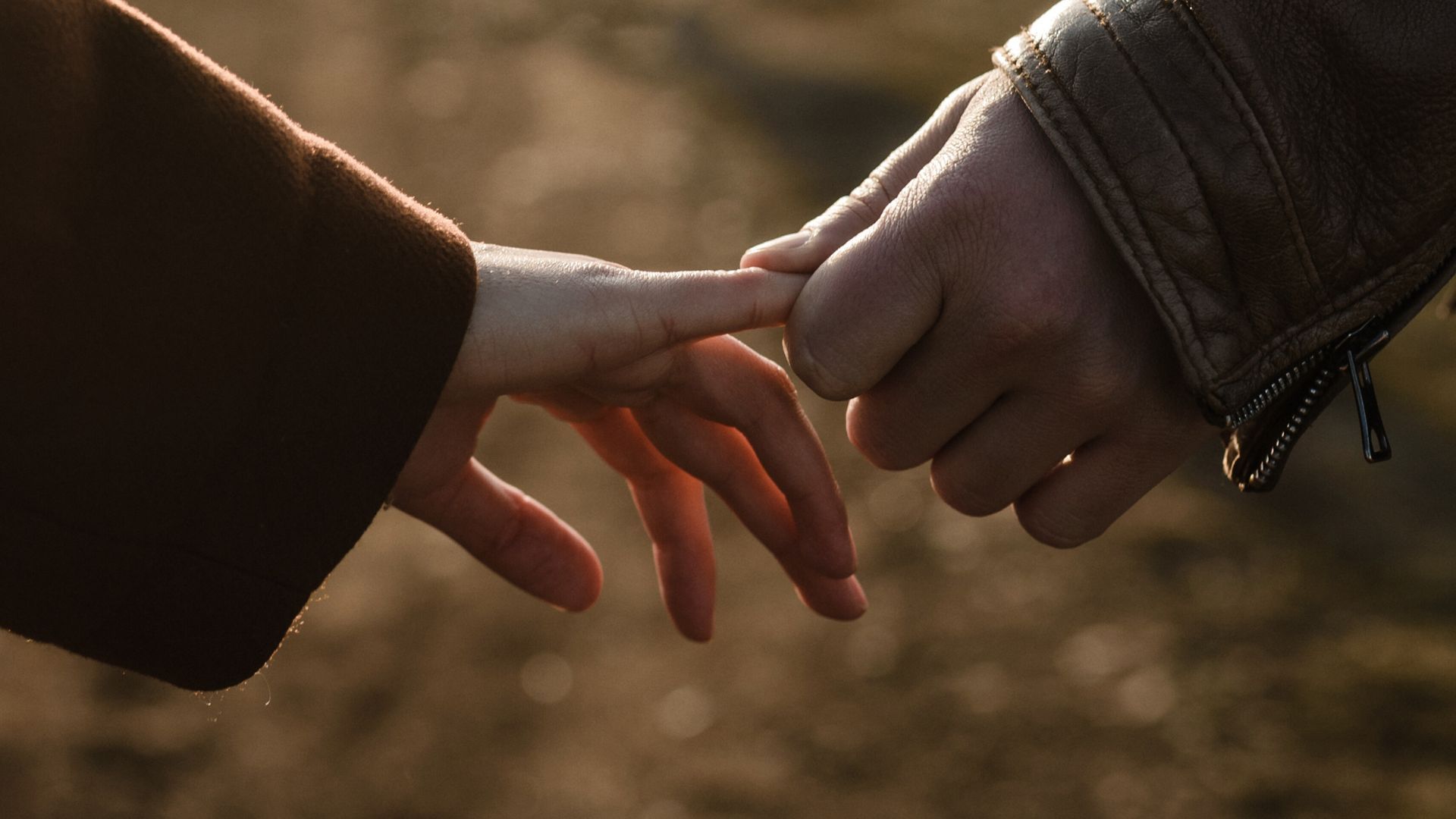 Adult hand holding a child's hand, symbolizing care. Skin tones vary, setting appears to be indoors with blurred background.