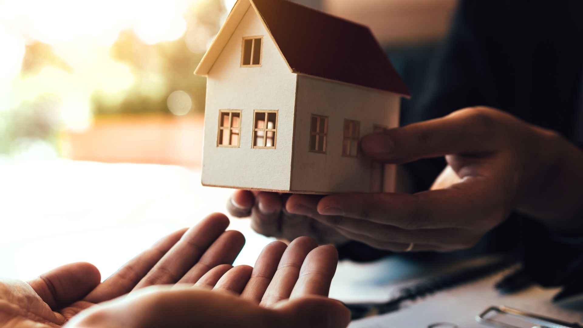 Hands exchanging a miniature house; a real estate transaction in sunlight.