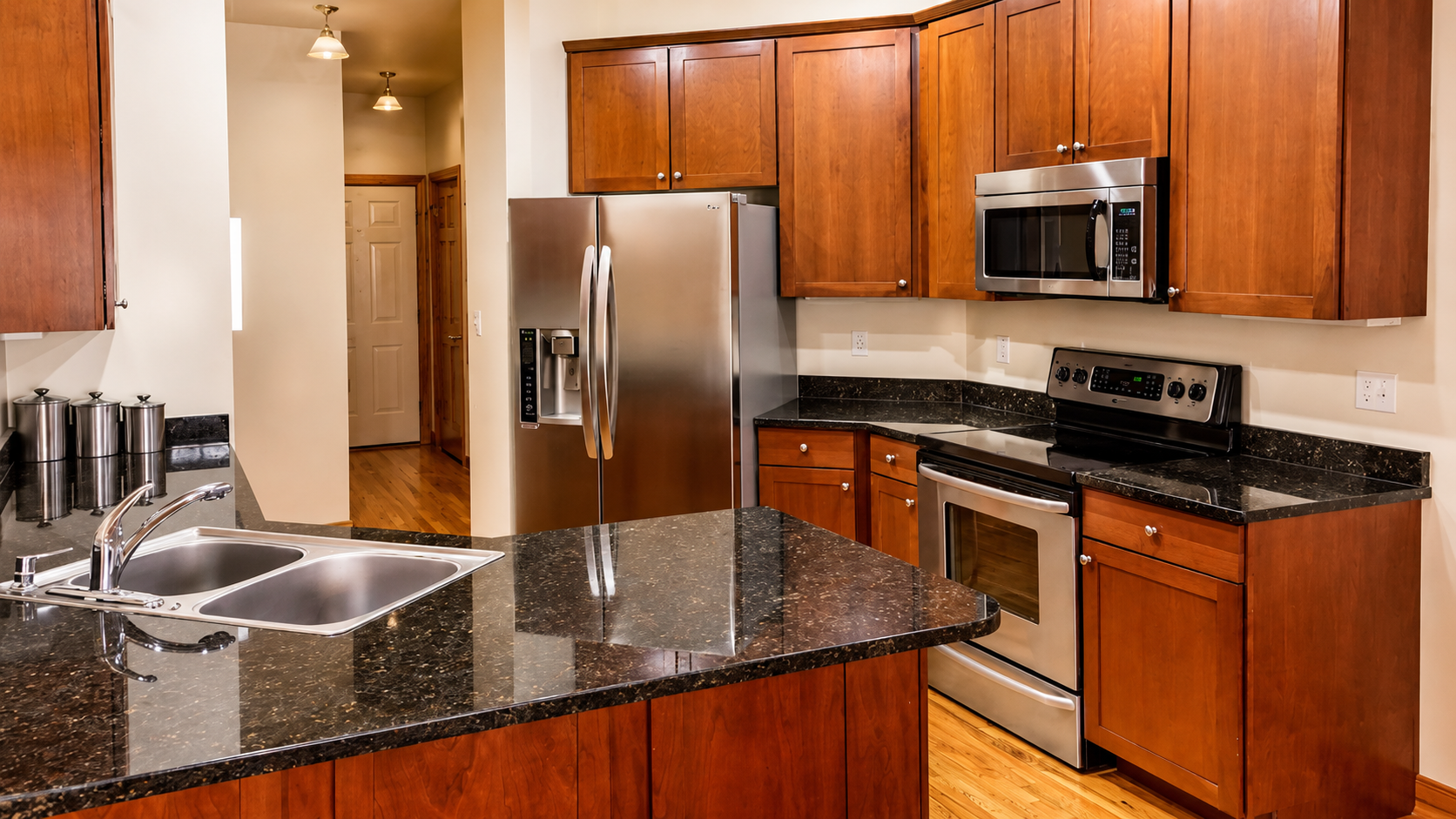 Modern kitchen with wood cabinets, stainless steel appliances, granite island, and double sink.