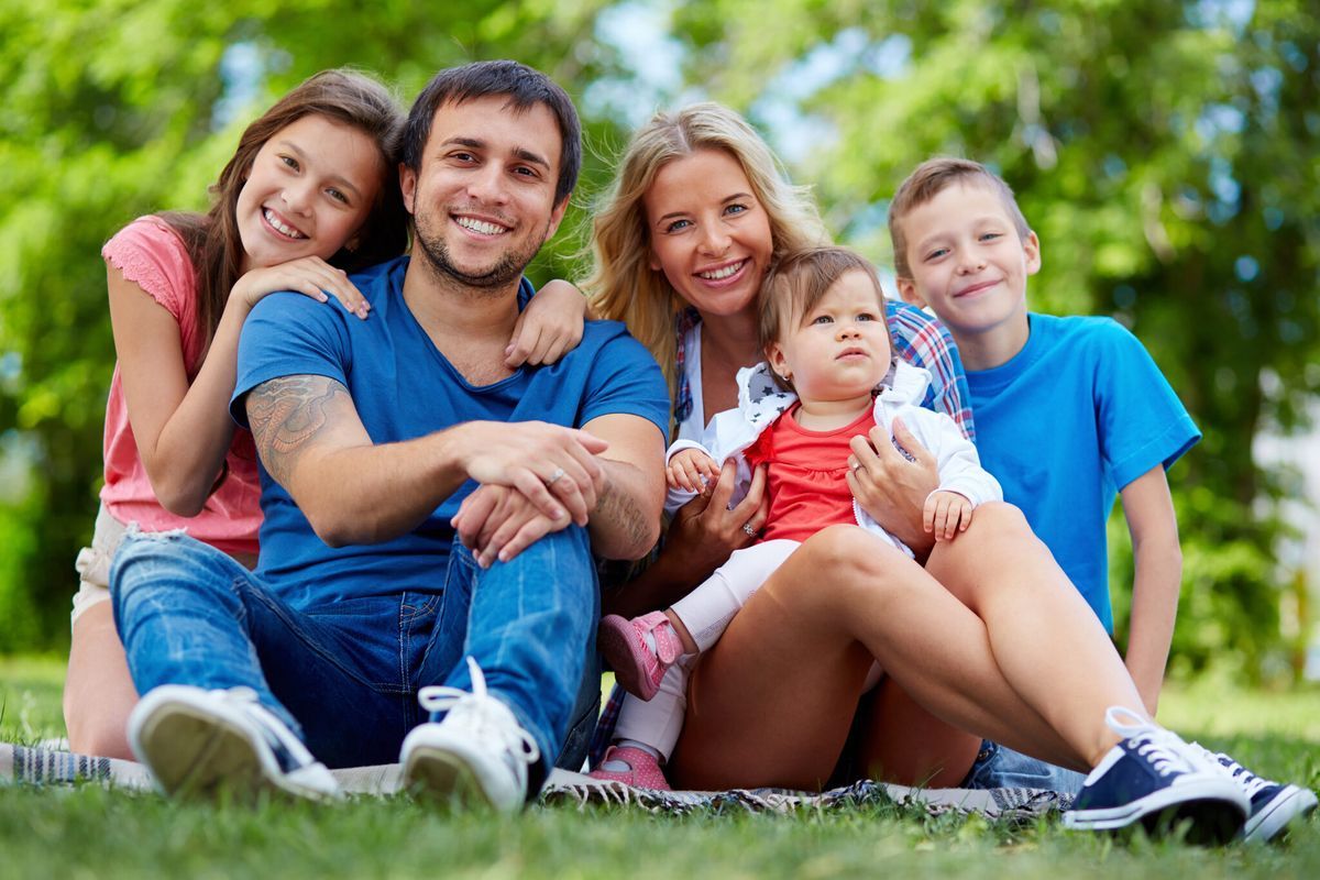 Five people sitting on grass in a park, smiling at the camera in bright blue shirts.